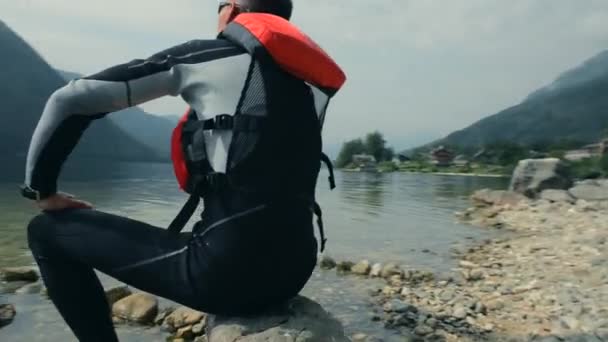 Kajakfahrer ruht sich am felsigen Seeufer aus. Sitzgelegenheiten und Aussicht genießen. — Stockvideo