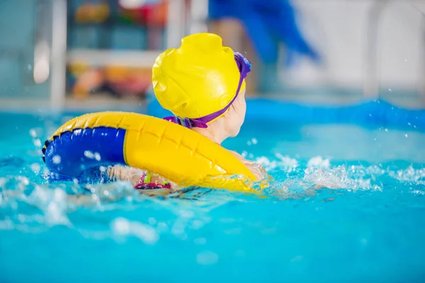 水上运动与娱乐主题 小女孩在黄色充气管内部的大室内游泳池游泳 戴着泳帽和护目镜 — 图库照片