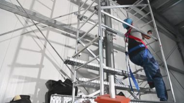 30 'lu yaşlarda Kafkasyalı müteahhit emniyet kemeri takıyor. Depo binasının içerisindeki havalandırma elemanlarını değiştirmek için iskeleyi kullanıyor..