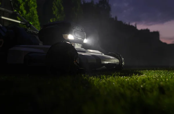 夏の終わりの夜の時間の間に裏庭の草の刈り取り Ledヘッドライト付き現代電気草の芝刈り機 — ストック写真