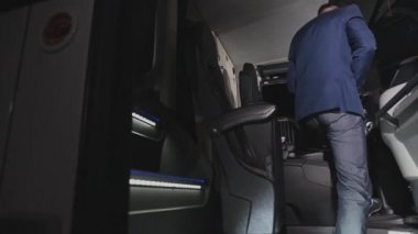 Özel koç operatörü takım elbiseli. Otobüse biniyor. Kulübeye oturuyor ve emniyet kemerlerini bağlıyor.. 