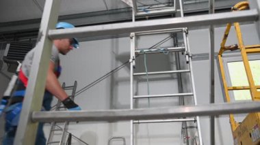 Beyaz erkek müteahhit koruyucu kayış ve sert şapka takarak Uzun Metal Merdiven 'e tırmanıyor..
