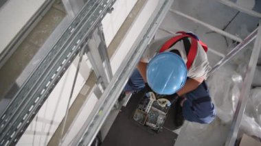 Erkek İnşaat İşçisi, yüksek bir platformda duruyor. Fındık cıvataları ve iş için gerekli diğer malzemelerle kutuları ayırıyor.. 