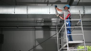 Beyaz erkek Hvac Müteahhiti Havalandırma Kuyusunda Metal Kıskaçlar Tavanda Birleştirildi. 