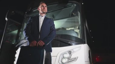 Beyaz tenli erkek gezgin, iş kıyafetleri içinde elinde bavuluyla gecenin geç saatlerinde büyük bir servis aracının önünde bekliyor.. 