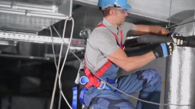 Çömelmiş Erkek HVAC Uzmanı Klima Sisteminin Borularındaki Siyah İzolasyonu Düzeltiyor. 