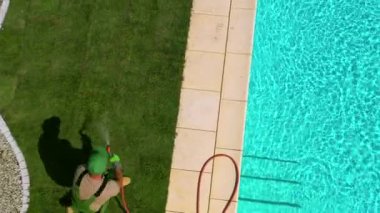 Bahçıvan yeni çimenler için çim biçiyor ve hortumla suluyor. Yeni Çim Kurulumunu Bitiren Adam Yüzme Havuzu Alanında. 