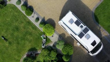 Çim biçme teknisyeni, karavanın yakınındaki lüks mahallede çim biçiyor. Otoparka park edilmiş.. 