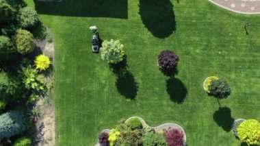 Geniş yeşil çimlerin ve özel evin arka bahçesindeki çoklu ağaçların ve bitkilerin havadan görünüşü. Bakım İşçisi Çimeni Kesiyor. 