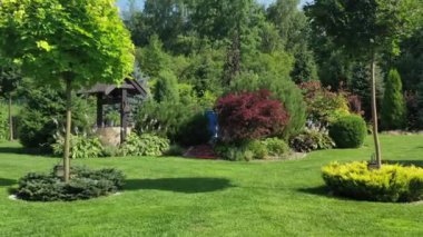 Parlak yeşil çimlerle çevrili çok renkli çalı bitkileri olan arka bahçe tasarımı. Erkek İşçi Çim Biçici. 