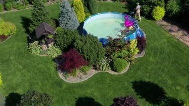 Yazın bol ve güzel tasarlanmış arka bahçe. Uzun ağaçlar, renkli çalılar ve orta büyüklükte yüzme havuzu olan bahçe manzarası. 