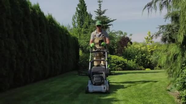 芝刈り機で芝を刈ることで私営不動産屋の定期メンテナンスを行う白人男性庭師 — ストック動画