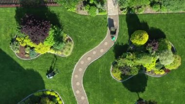 Büyük yeşil çimenlik ve kıvrımlı yoldaki bahçe bakım ekipmanları. Çalılıkları ve ağaçları olan adalar ahşap kuyu ve yerin üstünde yüzme havuzu. 