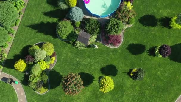 プールとカラフルな木々や茂みの複数のグループと巨大な住宅ヤードの空中ビュー 芝生と庭の世話をする男 — ストック動画
