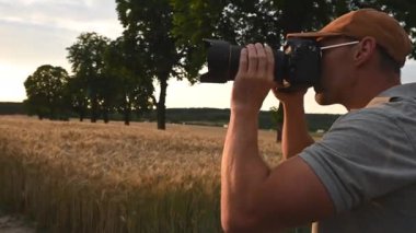 Profesyonel kameralı erkek fotoğrafçı öğleden sonra altın buğday tarlasının fotoğraflarını çekiyor.. 