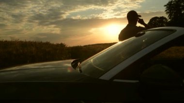 Üstü açık aracın yanında duran adam gün batımında geniş buğday tarlasının sakin kırsal manzarasını izliyor.. 