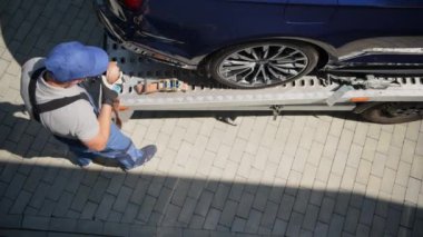 Araba galerisinden yeni alınmış bir araç Flatbed Truck 'tan indiriliyor. Sürücü Açılıyor ve Emniyet Kayışları Katlanıyor. 