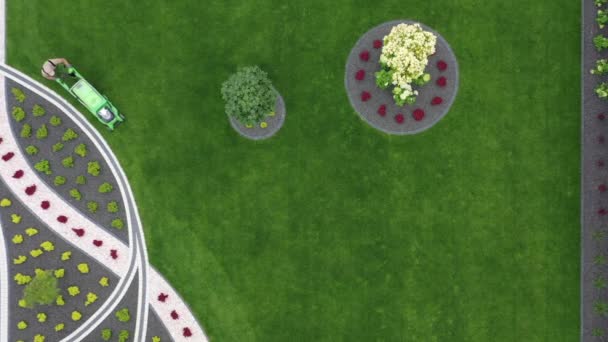 対称とカラフルな庭園の景観デザインの間に大きな緑の芝生を刈る男の上のビュー — ストック動画