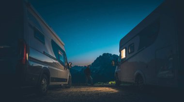 Kafasında el feneri olan 40 'lı yaşlardaki beyaz adamlar iki karavan arasında. Yüksek Dağlar Kamp Sahası Gece Kalıyor. RVing Caravaning TemasıName.