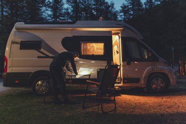 Caucasian Men in His 40s Browsing Local Map in Front of His RV Recreational Vehicle Camper Van During Colder Summer Evening. Camping Time Theme. clipart