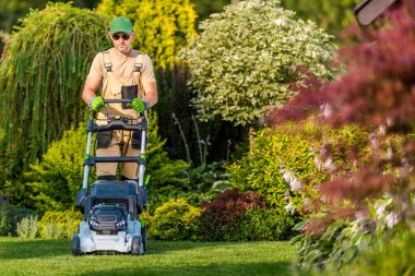 Elektrikli çim biçme makinesinin fişini kullanarak bahçesinde güneş gözlüğü takan beyaz adamlar. Yaz Bakkal Bakımı.