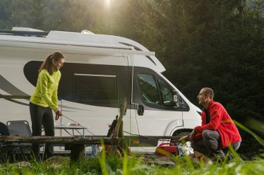 Motorlu Ev Tatil Aracı Tatil Zamanı Yolculuğu. Romantik Yaz Karavanı Van Camper Vahşi Yaşam Kampı. Kafkasyalı çift kamp ateşinin yanında eğleniyor..