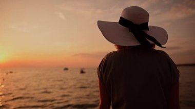 Sahne Günbatımı Yavaş Film Çekimi sırasında Deniz kenarında Büyük Güneş Şapkası Giyen Kadın. Turizm ve Seyahat Teması.