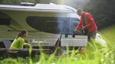 Genç çift kampta harika vakit geçiriyor. Yanan Kamp Ateşi, Yemek Pişirme ve Hayatlarının Keyfini Çıkarma. Karavan Motoru TemasıName.