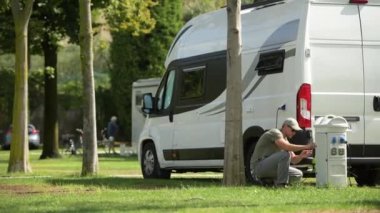 Kafkas erkekleri elektrik prizini modern karavan parkı bağlantı kulesine bağlıyor. Kamp Zamanı Teması.