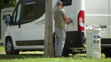 Kırklı yaşlarında Kafkasyalı bir tatilci elektrik prizini karavan parkına bağlıyor. Motorevi Özellikleri.