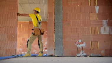 Kafkas İnşaat Müteahhiti Sarı Üniforma Giyiyor ve Beton Blokların İçinde Sert Şapka Binası Yapıyor. Endüstriyel Tema.