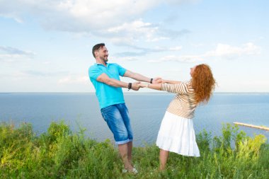 Genç iki göl ve gökyüzü arka plan üzerinde çim içinde sevgi dolu. Atış elele sakallı adam ve dans çayır çekici genç Kızıl saçlı kadın.