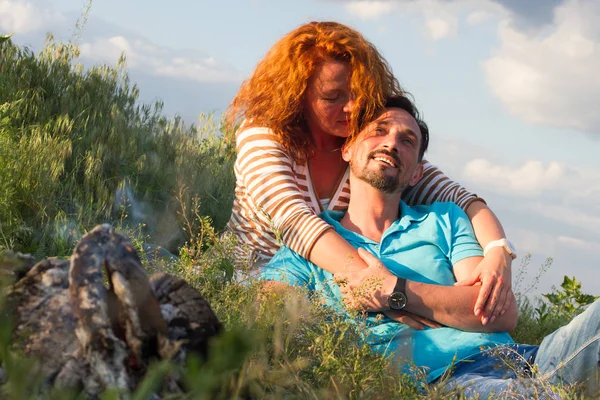 Portre, mutlu genç çift döşeme üzerinde battaniye şömine bulutlar arka plan üzerinde yakınındaki çimenlerin üzerinde