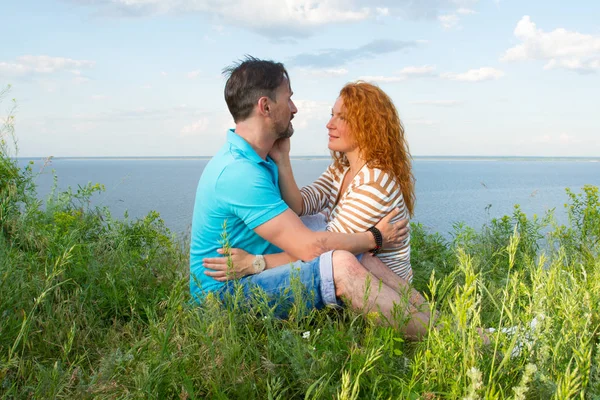 Birkaç aşk açık. Çim, çim Gölü kıyısında su ve gökyüzü arka plan üzerinde oturan sevgili sarıldı