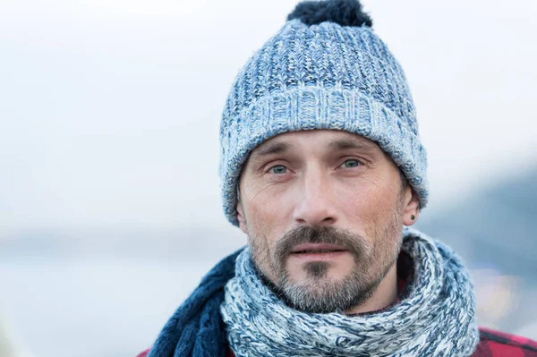 Portrait of white man in winter knitted hat and scarf. Urban white male on street in winter hat. Closeup of bearded guy in blue-white hat and scurf.