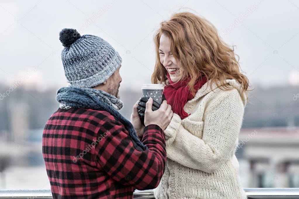 Happy woman and man hold craft glass of coffee. Smiling woman takes craft cup from guy in hat. Pare warm up hands by hot take away coffee. Urban life of urban people and warm drinks on street.