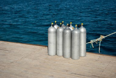 Dalış için hava ile sekiz silindir. sekiz alüminyum silindir Denizi üzerinde yerleştirin. Tam oksijen tankları rıhtımda. Mavi okyanus ve beyaz çelik silindir. Ahşap iskele üzerinde sekiz dalgıçlar Alüminyum tanklar closeup.
