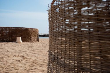 Örgülü rüzgar koruma kum Plajı kapatın. Sigara odak Rattan closeup koruma beyaz seramik pot ile dokunan. Güneşli kum plaj ve rattan rüzgar koruması