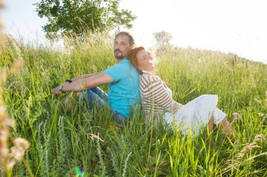 Birlikte oturup açık havada pikniğinde mutlu başarılı çekici çift. İnsanların yaz yeşil çim ormanında çimenlerin üzerinde çift. Kırmızı saçlı kadın arka arkaya yakışıklı sakallı adam oturuyor.