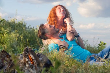 Mutlu genç çift çim şenlik ateşi başına oturmuş ve sarılma. Çift saatler seviyor