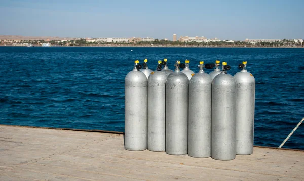 Group cylinders with helium on dock. ten white cylinders for divers on sea dock. oxygen tanks for divers on pier. Blue sea water and steel cylinders. Closeup of ten divers aluminum balloon on pier.