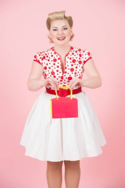 Genç güzel kız pembe bir arka plan üzerinde Studio izole kırmızı kutu tutar. Pin-up sarışın kadınla bukleler vermek için kutusu mevcut. Sarışın Bayan kırmızı noktalar ve beyaz etek. Hediye ile mutlu kız.