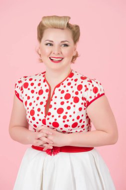 Pin-up saç ve makyaj holding silah, pembe arka plan izole dişler kocaman bir gülümseme ile çarpı işareti ile güzel çekici çekici kız portresi. Sarı bukleler ile mutlu sarışın kadın