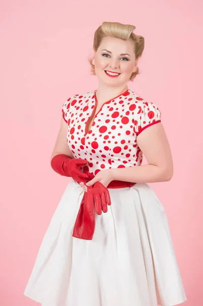 Pastel pembe bir arka plan üzerinde kırmızı uzun eldiven ile kız mutluluk sarışın. Pin-up makyaj studio izole kadınla güzel bukleler.