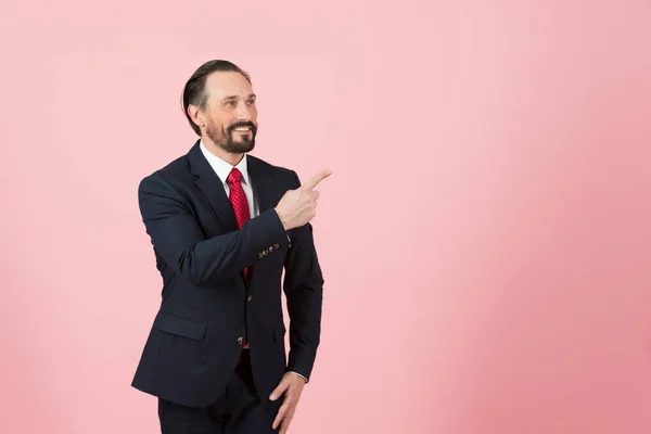 Handsome middle age man in suit and red tie pointing away side with his finger with pink rose background