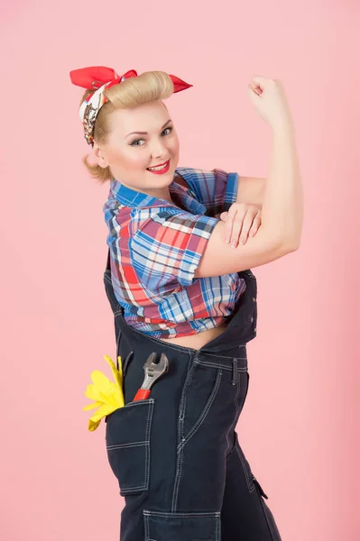 We Can Do It concept with blonde curls girl on pink background. Blonde Girl repairer with hand up. Woman can do styled concept isolated indoor. Pink pin up styled repairer.