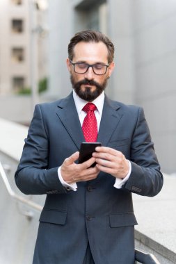 Arka plan binalarda gökdelenler ile kentsel City office dışı cep telefonu app manifatura kullanarak iş adamı. Genç Kafkas smartphone için iş iş tutan adam sakallı. İş için WiFi