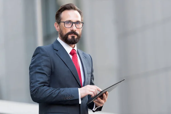 Portrait of businessman with tablet in hand on background of office building. Businessman using his tablet out of office with 4G. Young businessman touching digital tablet and checking financial data.