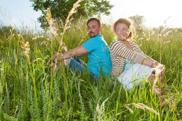 Couple in big green grass back to back. Man and woman sitting in the field in summer day. loving couple gently peacefully gossiping sits back to back in big field grass