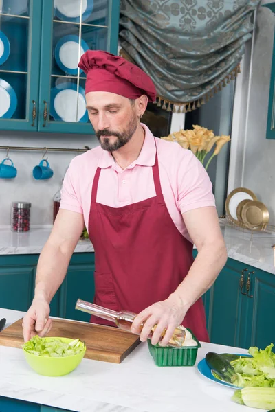 A man pours olive oil in bowl with fresh salad. Preparation of tasty and healthy food. Cooking and home concept - close up of male hands flavouring salad in a bowl with olive oil